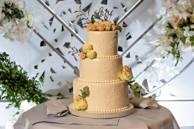 Üç katlı, çiçekli bir düğün pastası ve baş harfli bir aşk işareti.