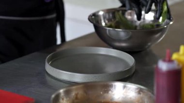 Siyah eldivenli biri metal tepside yemek hazırlıyor.