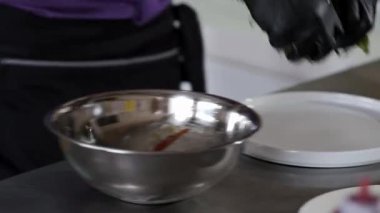 Siyah eldivenli biri metal bir kasede yemek hazırlıyor.