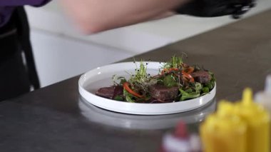 Siyah eldivenli biri tabakta salata hazırlıyor.