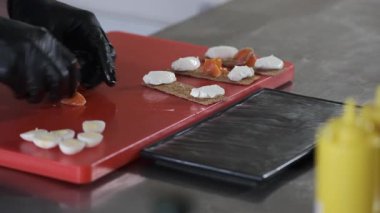 Siyah eldivenli biri kırmızı kesme tahtasında yemek hazırlıyor.