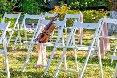 Bir keman beyaz katlanır sandalyelerin ortasında bir sandalyede oturur..