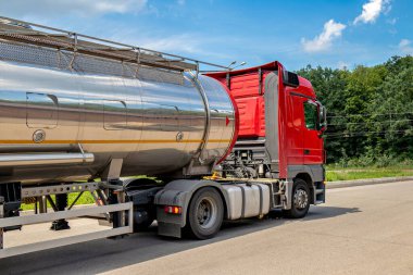 Yolunda gümüş bir tanker taşıyan büyük kırmızı bir kamyon...