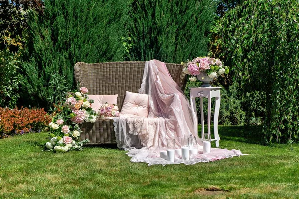 Hasır bir sandalye, çiçek aranjmanları ve vazo çiçekli bir masa..