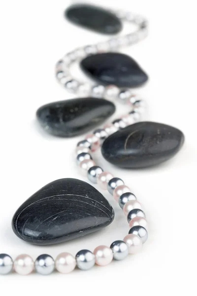 Perlenkette zwischen schwarzen Kieselsteinen auf weißem Hintergrund — Stockfoto