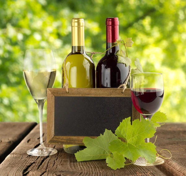 Şarap şişeleri ve ahşap masa üzerinde küçük yazı tahtası — Stok fotoğraf