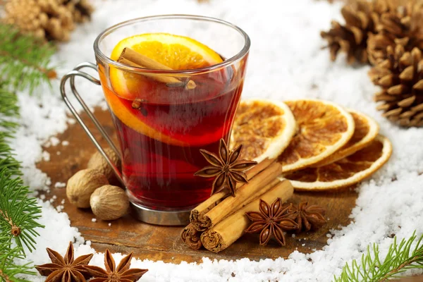 Glass of mulled wine, spices and snow on wooden table — Stock Photo, Image