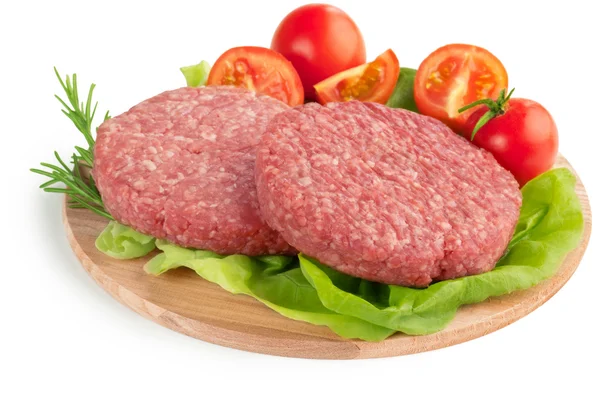 Raw burgers, tomatoes and lettuce on wooden cutting board — Stock Photo, Image