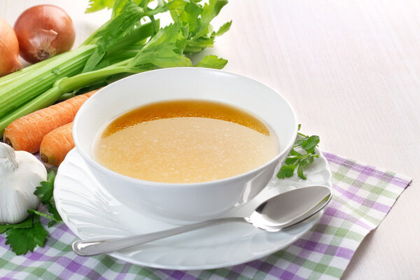 Bowl of broth and fresh vegetables on wooden table