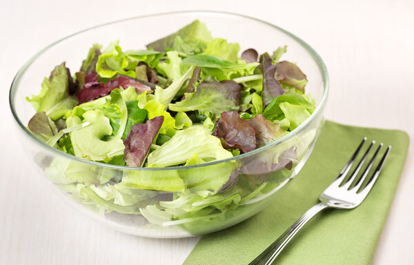 Bowl of mixed salad, fork and napkin on beige table