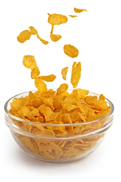 Cornflakes vallen in een glazen kom op witte achtergrond — Stockfoto