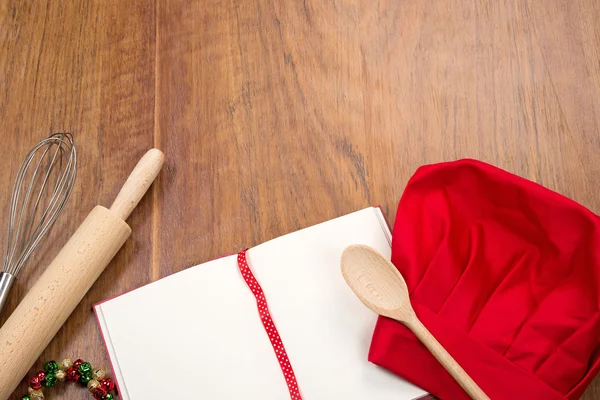 Open cookbook, chef's hat and kitchen tools on wood table — 图库照片