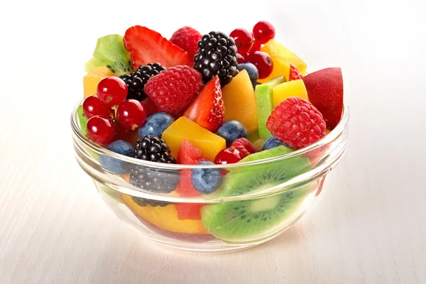 Fresh fruit salad in glass bowl isolated on beige wood table — Zdjęcie stockowe