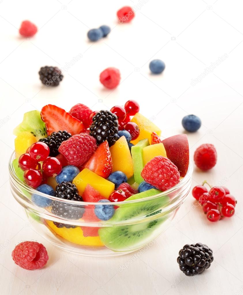 Bowl of fruit cocktail and mixed berries scattered on wooden table