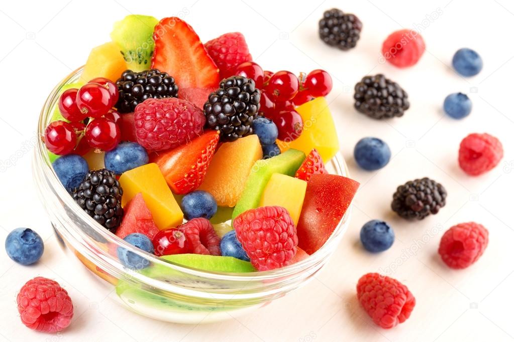 Close up of bowl with fruit cocktail and mixed berries scattered