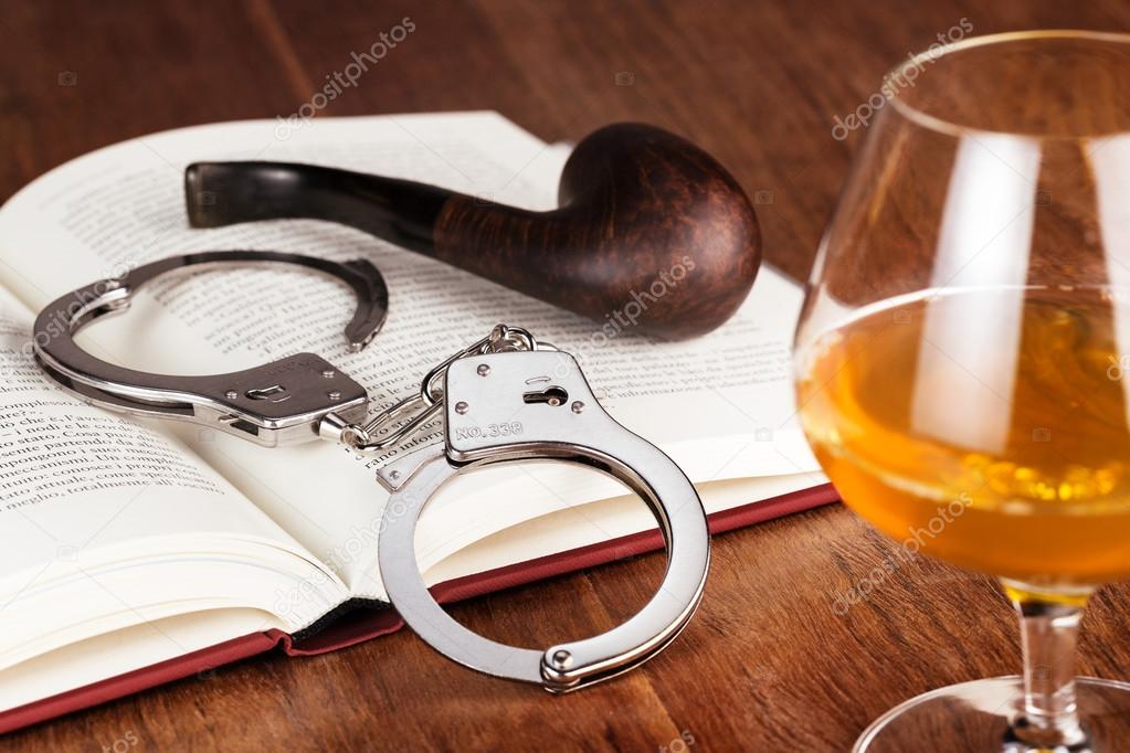 glass of liquor, handcuffs and pipe on open book