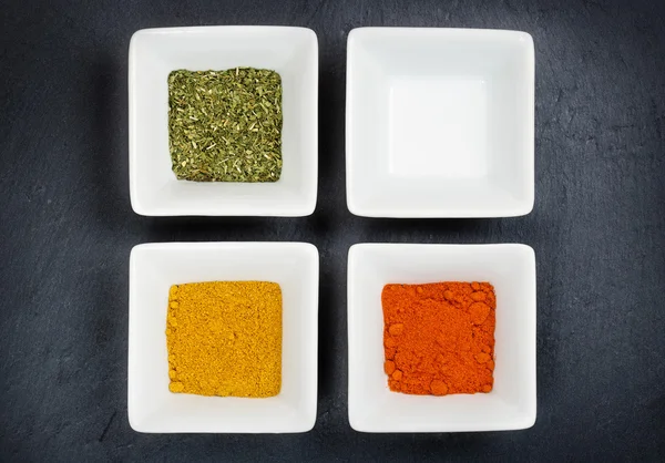 Three bowls with spices and a blank one on grey background — Stock Photo, Image