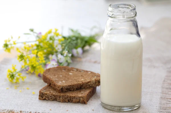 Bottle of milk, rye bread and summer flowers — Stock fotografie