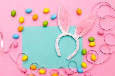 Paskalya tavşanı. Mutlu Paskalya tatili arka plan kavramı. Düz, ofis masasındaki modern kırsal pembe pastel kağıtta kutlama için aksesuarlı renkli tavşan yumurtası yatıyordu..