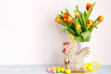 Beyaz arka planda boyanmış Paskalya yumurtaları ve beyaz sürahi içinde sarı taze laleler..