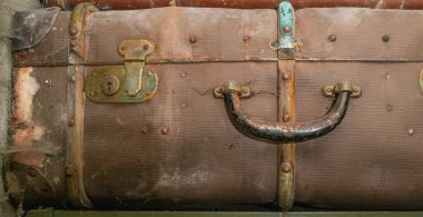 Terk edilmiş garajdaki bir rafta eski model bavullar. Kilit ve sapta aşınma var. Duvarlarda toz ve örümcek ağları.