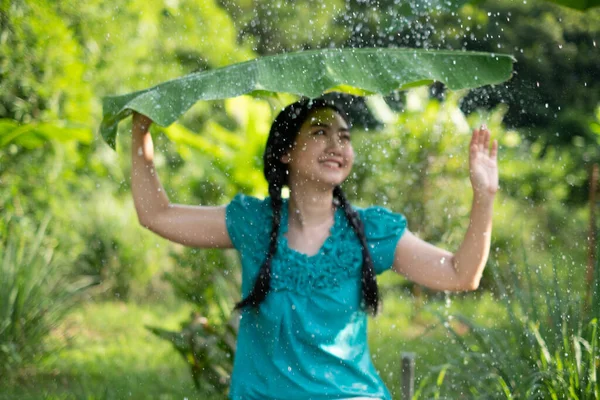 緑の庭で雨の中でバナナの葉を保持黒髪の若いアジアの女性のぼやけたイメージの肖像画背景 — ストック写真