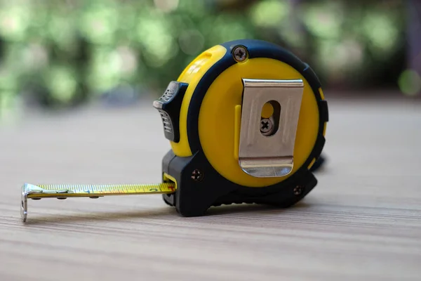 Yellow tape measure on wooden board at blurred background