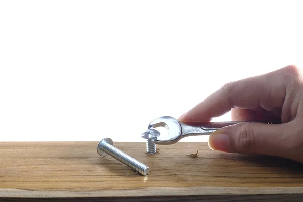 Close-up of a joiner hand with a wrench screwing a furniture screw into a wooden plank at white background, The effort  wrong of tools as a fail concept