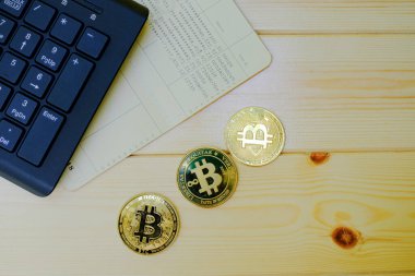 Banka hesap defterindeki altın Bitcoin paralarını ahşap masada dizüstü bilgisayarlı klavyeyle kapat