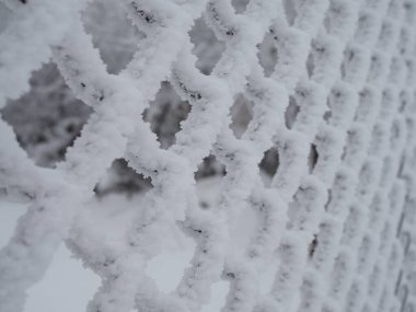 Yakın çekimde, hücrelerde kalın bir kar tabakasıyla kaplı metal ağ.