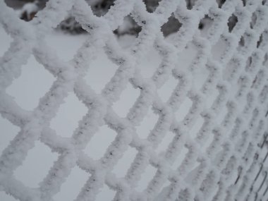 Yakın çekimde, hücrelerde kalın bir kar tabakasıyla kaplı metal ağ.