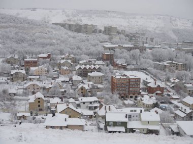Karla kaplı şehir ve ufuktaki kentsel evler bulutlu kış gününde görünüyor..