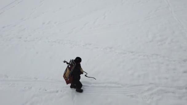 El hombre con taladro de hielo y bolsa de pesca con equipo está caminando sobre hielo congelado grueso. Pesca de invierno. Pescador en lago congelado — Vídeos de Stock