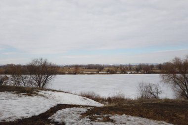 İlkbaharın başlarında kırsal alanda. Ön planda, karın altında bir nehir.