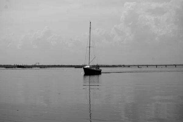 夏日里 平静的天气里 用船载马达在水面上飘扬着的有芦苇帆的老游艇 在森林海岸上的后视镜 以及多云的天空背景 — 图库照片