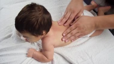 Masör bebeğe bir masaj yapar. Masaj yapılan bir çocuk kanepede yatıyor. İç çamaşırlı bebek. Bir çocuğun hayatındaki ilk masaj. Yukarıdan görünüşü.