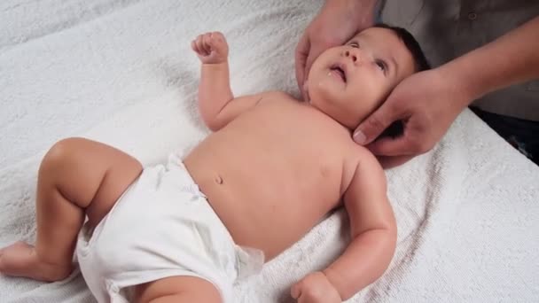 Der Masseur massiert das Baby. Ein Kind, das massiert wird, liegt auf der Couch. Baby im Slip. Die erste Massage in einem Kinderleben. Der Blick von oben. — Stockvideo