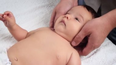 Erkek doktorlar bebeğe el masajı yapar. Masaj yapılan bir çocuk kanepede yatıyor. Bir çocuğun hayatındaki ilk masaj. Kapat.