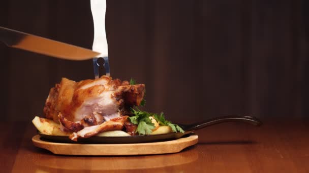 Une main d'homme coupe un plat de viande appétissant dans l'os avec un couteau. Plat de viande prêt avec garniture dans une poêle. Poignée sur un fond en bois. Mouvement lent — Video