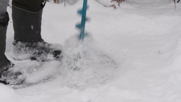 Perforando hielo con un taladro de hielo. Perforando agujeros en el hielo. Preparación antes de la pesca de invierno. Piernas en botas mientras perfora hielo. Movimiento lento. — Vídeo de stock