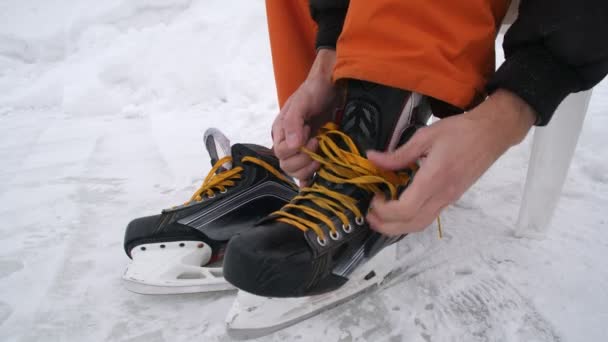 Мужские руки затягивают шнурки на коньках. Хоккейные коньки с ярко-желтыми шнурками. Подготовка к катанию на лыжах по заснеженному льду. — стоковое видео