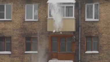 Ağır çekimde çatıdan düşen kar. Çok katlı bir binanın çatısından beyaz kar atıyorlar. Ağır mevsimlik erkek işçilik. Aşırı kardan çatıyı temizliyorum..