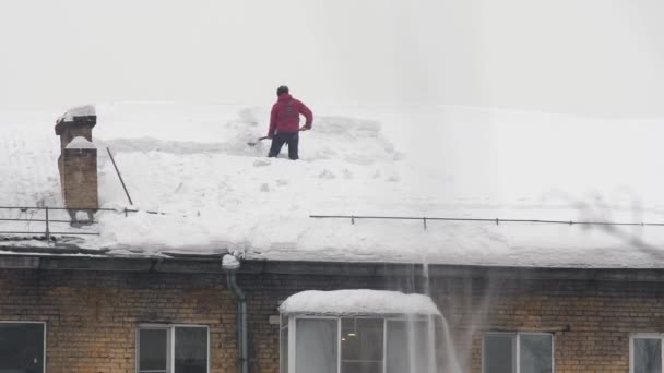 Os trabalhadores jogam a neve branca do telhado de um edifício de vários andares. Trabalho masculino sazonal pesado. As pessoas trabalham como uma pá. Limpeza do telhado de excesso de neve. — Vídeo de Stock