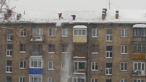 Los trabajadores tiran nieve blanca desde el techo de un edificio de varios pisos. Trabajo masculino estacional pesado. La gente trabaja como una pala. Limpiando el techo del exceso de nieve. Movimiento lento — Vídeos de Stock