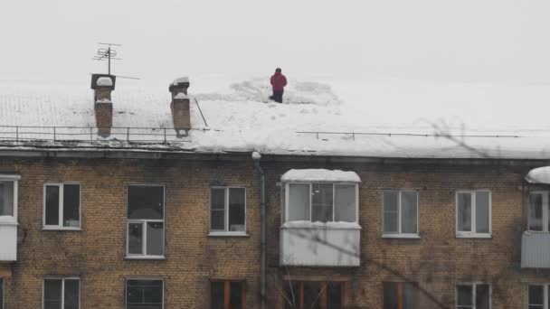 Les travailleurs jettent de la neige blanche du toit d'un immeuble de plusieurs étages. Main-d'œuvre masculine saisonnière. Les gens travaillent comme une pelle. Nettoyage du toit de l'excès de neige. Mouvement lent — Video