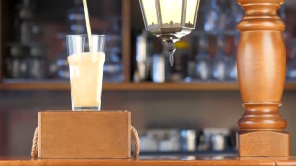 Bier in ein durchsichtiges Glas auf der Theke gießen. Leichtes, goldenes Bier ergießt sich vor der Kulisse einer Kneipe in ein Glas. — Stockvideo