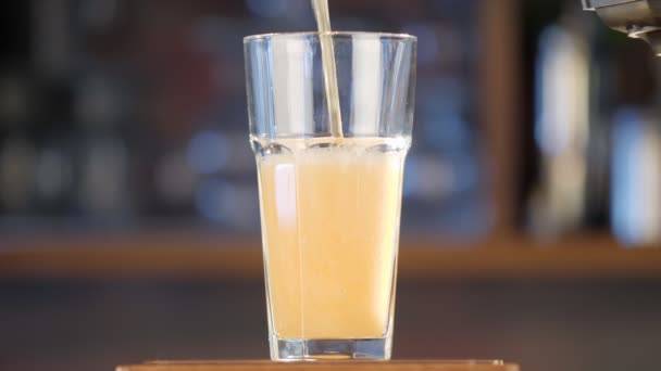 Bier in ein durchsichtiges Glas auf der Theke gießen. Vor der Kulisse einer Kneipe ergießt sich leichtes, goldenes Bier in ein Glas. Nahaufnahme. — Stockvideo