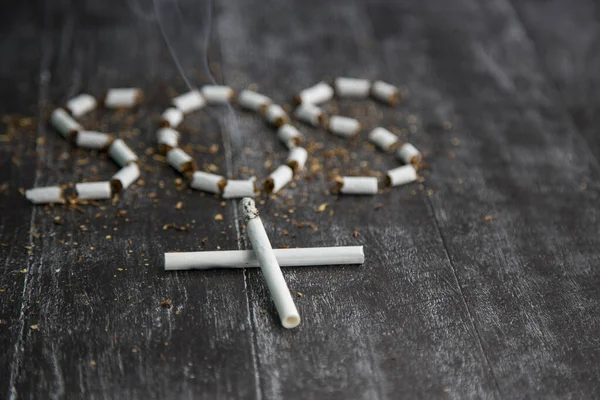 the ash and cigarette look like a cross, an artistic concept for world no tobacco day. Sign SOS of tobacco. Health risks of nicotine. The cigarette kills. black and white dark photo