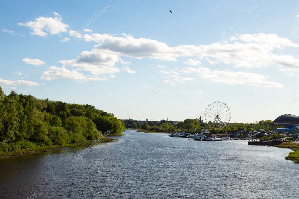 Panorama of the landscape from the embankment of the wide river, blue sky, white clouds, Ferris wheel in the background. Yaroslavl, Russia, city center