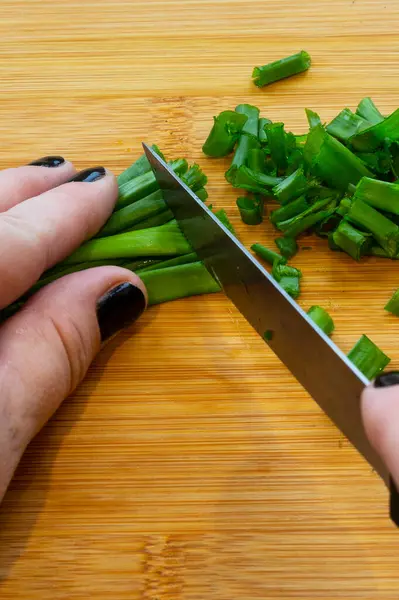 Ženské ruce s nožem, krájení zeleniny na dřevěné desce. žena krájí zelenou cibuli — Stock fotografie